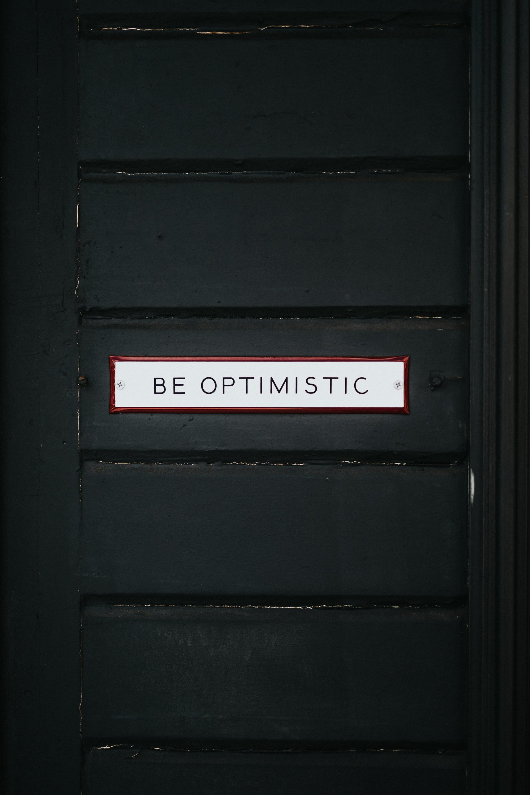 Black wooden door with be optimistic text overlay