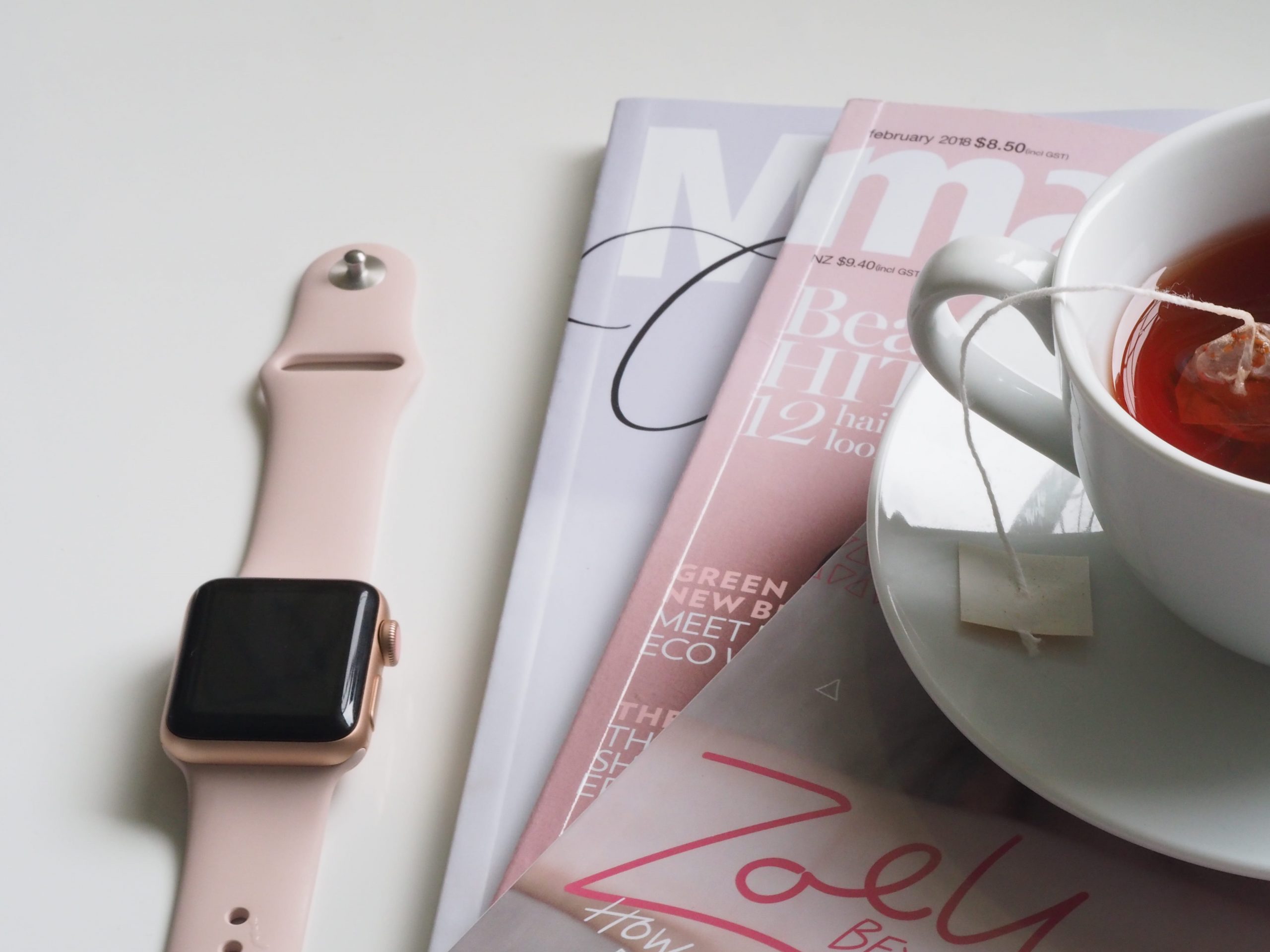 rose gold aluminum case Apple Watch with pink Sport Band beside white ceramic teacup filled with red liquid placed on white wooden board
