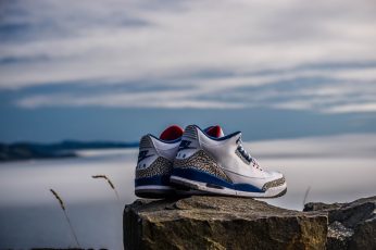 Wallpaper pair of white-and-blue Air Jordan 2’s on rock fragment, pair of white-black-and-blue Nike Air shoes on top of rock at daytime