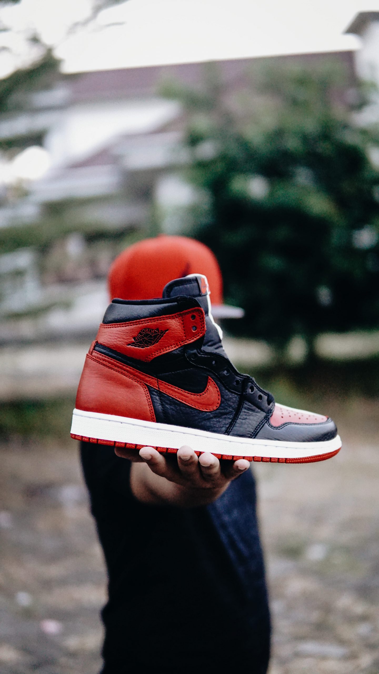 Wallpaper selective focus photo of person holding unpaired black and red Nike Air Jordan 1 shoe