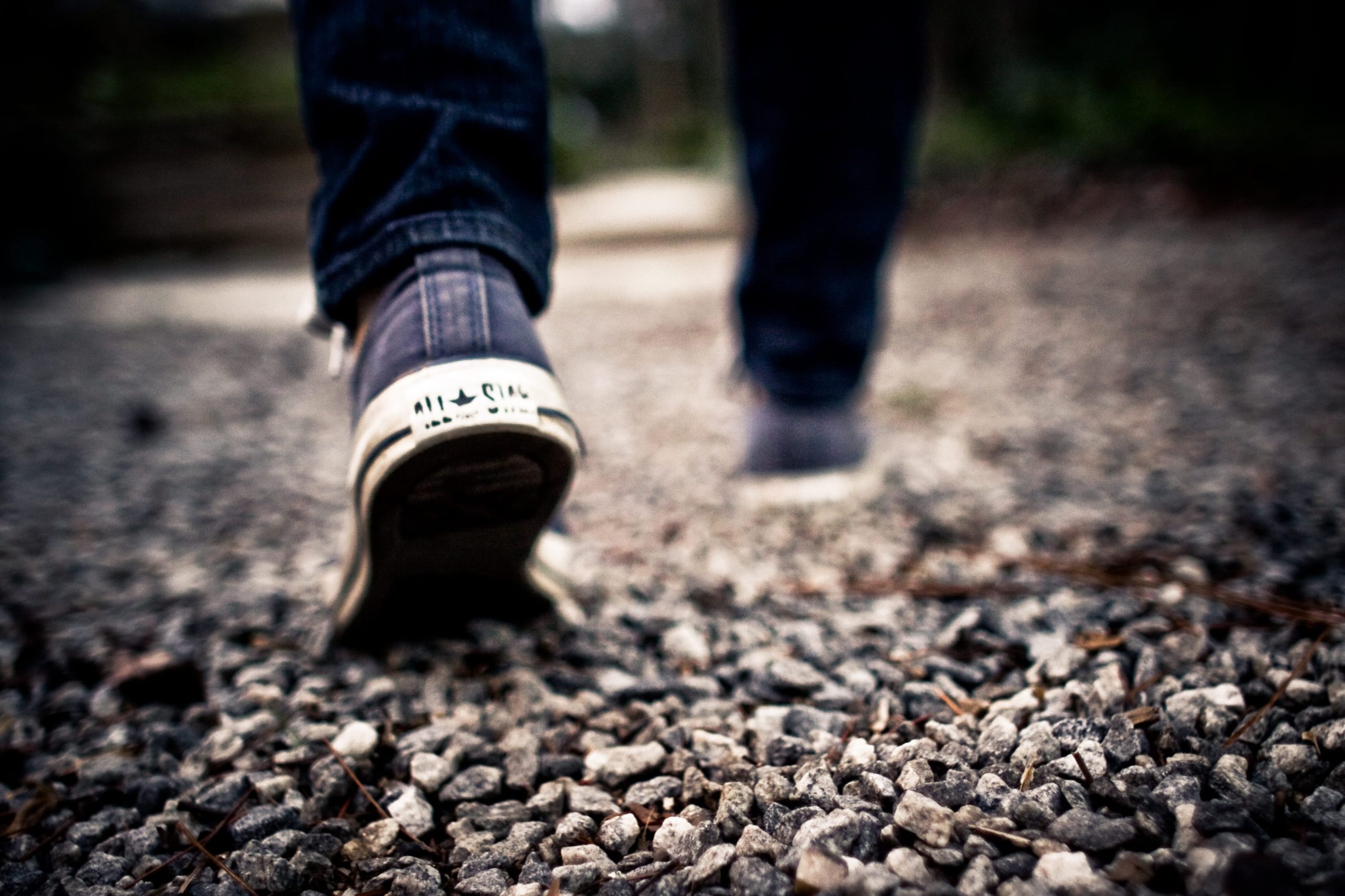 Man wearing blue-and-white Converse low-top sneakers walking on rock road wallpaper