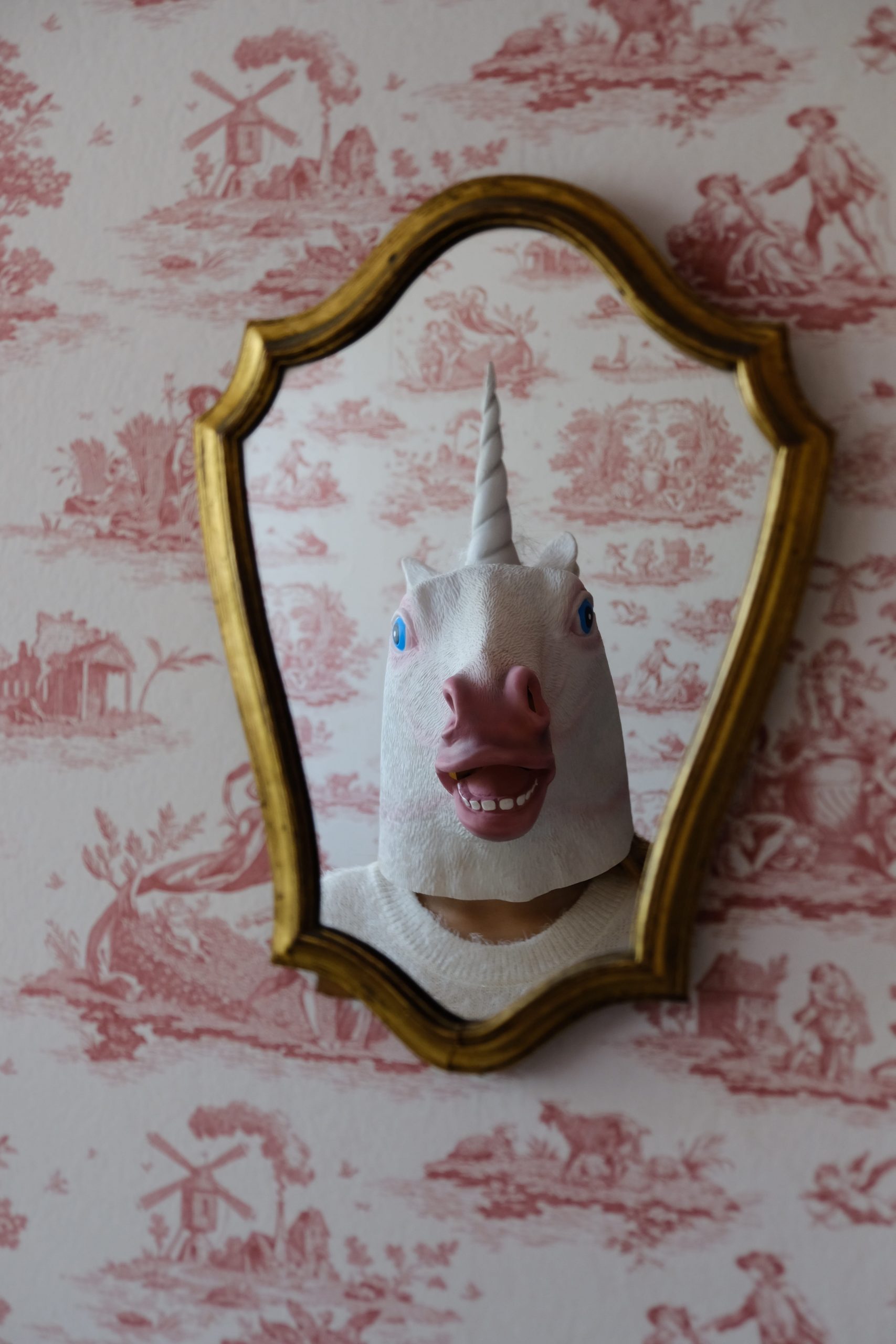 Person with white unicorn mask stands in front of wall mirror wallpaper